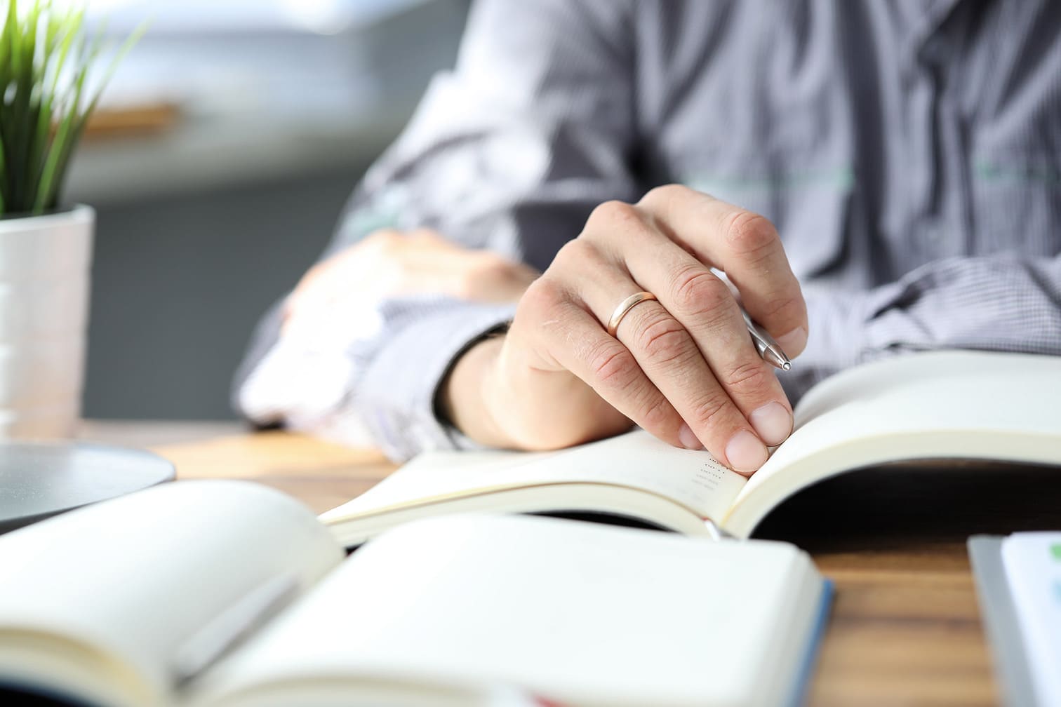 Handen van een man op een opengeslagen boek aan een bureau als symbool voor kennis en advies
