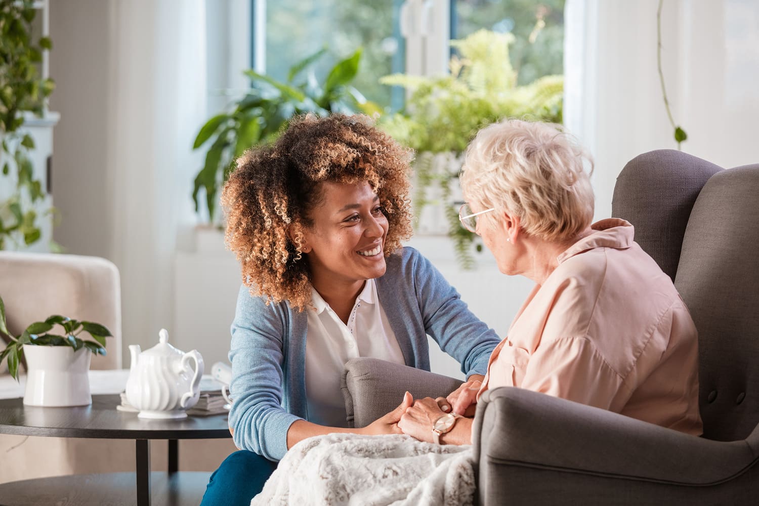 Vrouwelijke begeleidster in een warm gesprek met een oudere vrouw in een fauteuil